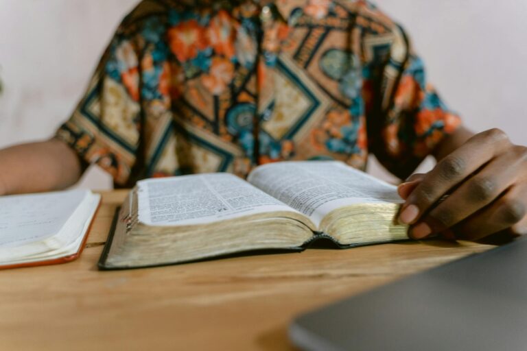 Man in colorful shirt reads an open book on a wooden table, focusing on study.
